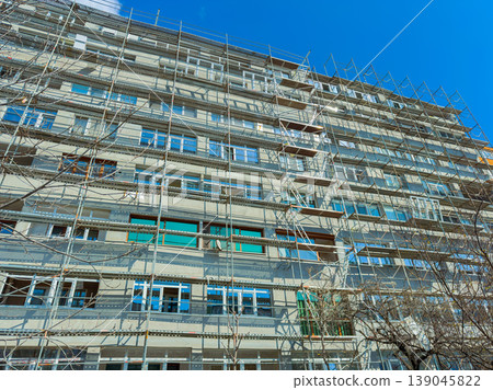 Construction work is taking place on a large building with scaffolding under a clear blue sky during daytime in an urban area Construction work is taking place on a large building with scaffolding under a clear blue sky during daytime in an urban area 139045822