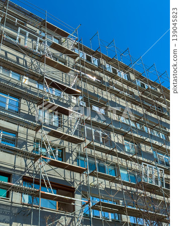Construction work on a multi-story building with scaffolding under a clear blue sky during the day Construction work on a multi-story building with scaffolding under a clear blue sky during the day 139045823