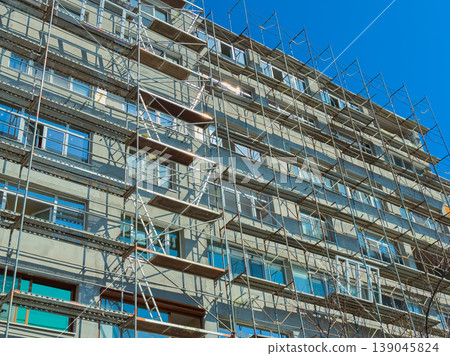 Building renovation project takes place in urban area with scaffolding set up for workers to access higher levels of the structure Building renovation project takes place in urban area with scaffolding set up for workers to access higher levels of the structure 139045824
