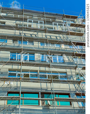Construction workers build a new apartment building in the city with scaffolding around the structure on a sunny day Construction workers build a new apartment building in the city with scaffolding around the structure on a sunny day 139045825