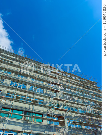 Building renovation with scaffolding under a clear blue sky in a city setting during daytime hours Building renovation with scaffolding under a clear blue sky in a city setting during daytime hours 139045826