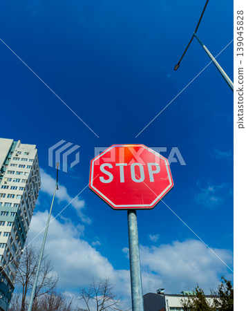 Stop sign stands tall under blue sky with white clouds in a city scene during daytime near buildings and streetlights Stop sign stands tall under blue sky with white clouds in a city scene during daytime near buildings and streetlights 139045828