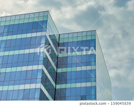 Modern building with glass facade and cloudy sky in the background of a city during the day capturing urban architecture and design Modern building with glass facade and cloudy sky in the background of a city during the day capturing urban architecture and design 139045839