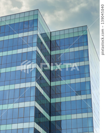 Building shaped with glass panels showing clear reflections under a cloudy sky in an urban setting during daytime hours Building shaped with glass panels showing clear reflections under a cloudy sky in an urban setting during daytime hours 139045840
