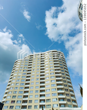 Sky view of a tall residential building with many windows against a backdrop of clouds and blue sky in an urban area during the day Sky view of a tall residential building with many windows against a backdrop of clouds and blue sky in an urban area during the day 139045852