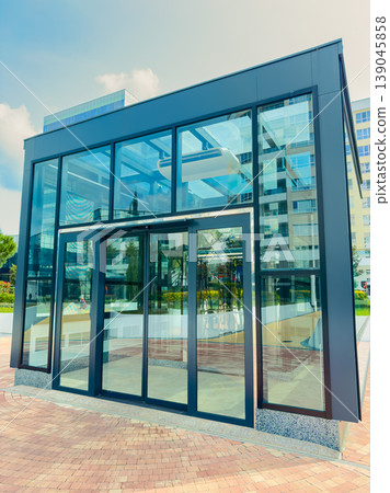 Modern glass building located in a city area showcases a sleek design with large windows in bright daylight surrounded by urban greenery Modern glass building located in a city area showcases a sleek design with large windows in bright daylight surrounded by urban greenery 139045858