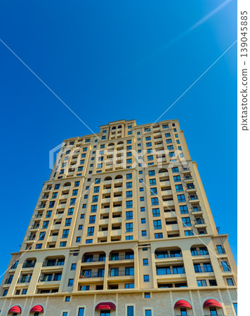 Tall building stands under clear blue sky in urban area with open balconies and modern design, showcasing architectural details and the structure's height Tall building stands under clear blue sky in urban area with open balconies and modern design, showcasing architectural details and the structure's height 139045885