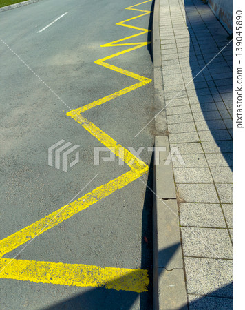 Yellow zigzag line on the road signals caution near the sidewalk during daytime at an urban location Yellow zigzag line on the road signals caution near the sidewalk during daytime at an urban location 139045890