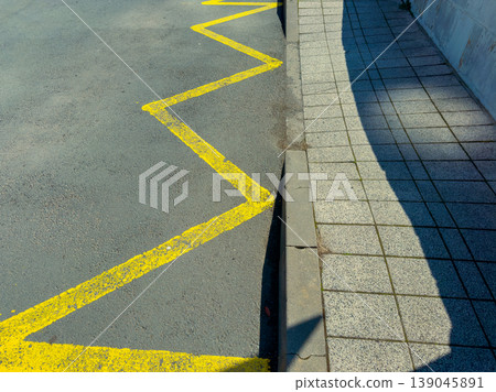 Zigzag yellow line on pavement next to sidewalk in urban area during daylight showing urban design and boundary marking Zigzag yellow line on pavement next to sidewalk in urban area during daylight showing urban design and boundary marking 139045891