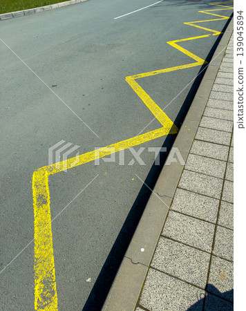 Curved yellow line marking zigzag pattern on asphalt near sidewalk in a public area on a sunny day Curved yellow line marking zigzag pattern on asphalt near sidewalk in a public area on a sunny day 139045894
