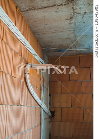 Wire is connected to brick wall in construction site with some exposed surfaces and tools around during daylight hours Wire is connected to brick wall in construction site with some exposed surfaces and tools around during daylight hours 139045905