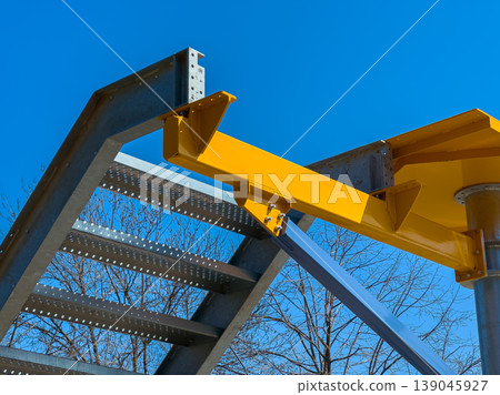Construction site shows metal structure with yellow support beam on steel staircase under clear blue sky in daytime 139045927