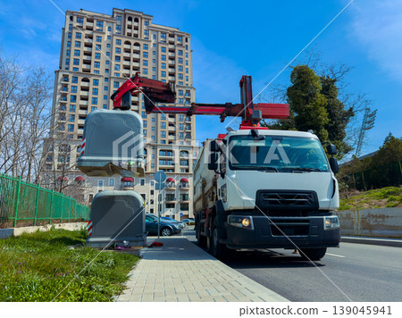 Truck collects waste from containers on a busy city street with a tall building in the background on a clear day 139045941
