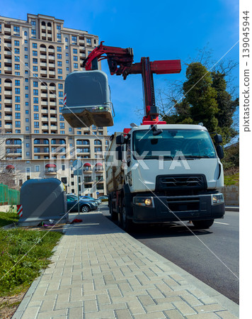 Garbage truck removes waste containers on city street during clear day 139045944