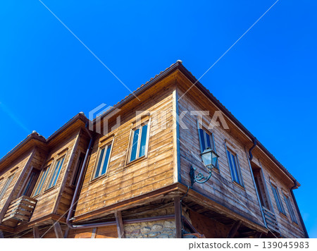Historic wooden house with five windows under a clear blue sky located in a village setting during daylight hours Historic wooden house with five windows under a clear blue sky located in a village setting during daylight hours 139045983