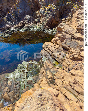 Rocky shoreline near water with clear reflections and bright sunshine on a clear day in coastal area Rocky shoreline near water with clear reflections and bright sunshine on a clear day in coastal area 139045994