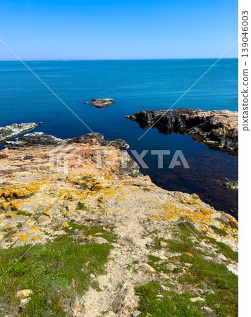 View of rocky coastline and calm sea under clear blue sky during daytime at a coastal location View of rocky coastline and calm sea under clear blue sky during daytime at a coastal location 139046003