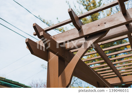 Wooden structure is seen against the sky in a garden, showing details of beams and support frames during daytime 139046031