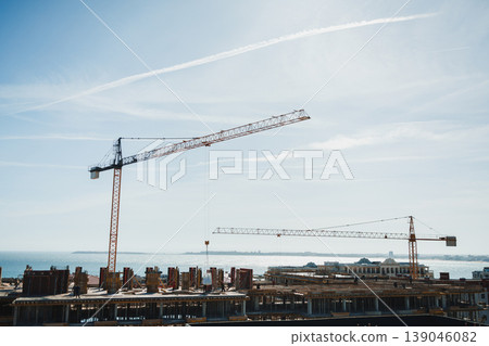 Construction site with cranes and new building under development near the coast during daylight hours Construction site with cranes and new building under development near the coast during daylight hours 139046082
