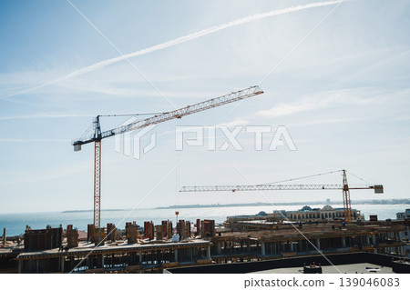 Construction work takes place near a body of water with cranes and buildings under development during bright daylight 139046083
