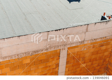 Construction work on a building showing an unfinished wall and a roof under sunlight in an urban area during midday Construction work on a building showing an unfinished wall and a roof under sunlight in an urban area during midday 139046091
