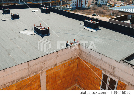 Construction site shows new roof installation on building with unfinished walls and nearby structures in background during bright daylight Construction site shows new roof installation on building with unfinished walls and nearby structures in background during bright daylight 139046092