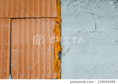 Construction site shows wall made of orange bricks and gray concrete with mortar filling in the gaps during day 139046098