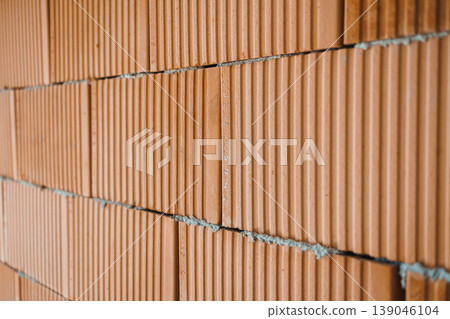 Brick wall construction showing orange bricks stacked with mortar, indicating building work taking place in an urban setting during daylight hours 139046104