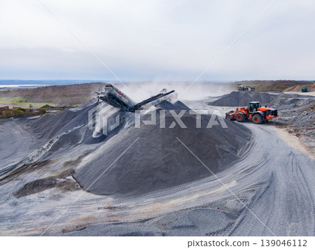 Granite quarry operation showing heavy machinery and stone piles at work during cloudy day Granite quarry operation showing heavy machinery and stone piles at work during cloudy day 139046112