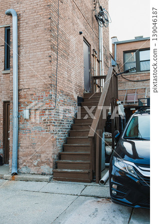 Stairs lead to a door behind a brick building in an urban area with a parked car nearby Stairs lead to a door behind a brick building in an urban area with a parked car nearby 139046187