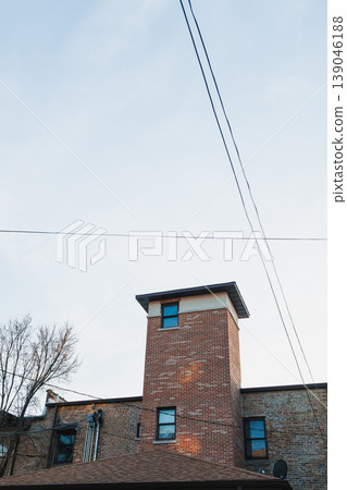 View of a brick building with a tower and clear sky during the day in an urban area, showcasing the architecture and nearby trees and power lines View of a brick building with a tower and clear sky during the day in an urban area, showcasing the architecture and nearby trees and power lines 139046188