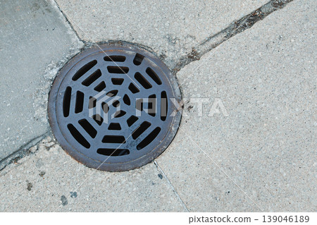 Drain cover on concrete sidewalk with pattern seen on a sunny day in the city Drain cover on concrete sidewalk with pattern seen on a sunny day in the city 139046189