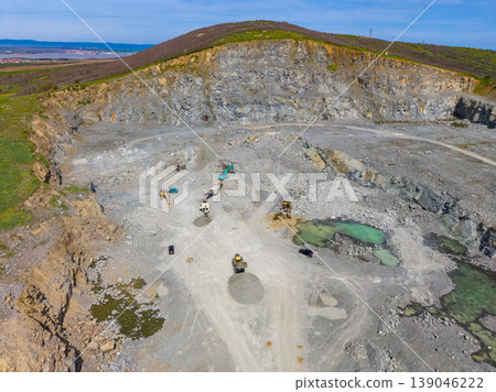 Granite quarry in operation with machinery and workers completing tasks under clear skies in an open landscape 139046222