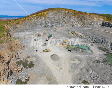 Granite quarry with heavy machinery working on stone extraction and processing in a large open pit area during daytime hours Granite quarry with heavy machinery working on stone extraction and processing in a large open pit area during daytime hours 139046223