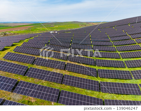 Solar panels line a large field in an open area with green hills in the background on a clear day with blue sky Solar panels line a large field in an open area with green hills in the background on a clear day with blue sky 139046247