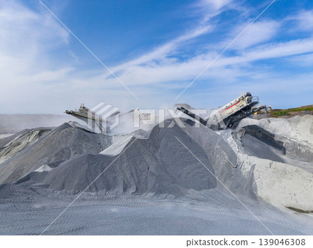 Granite quarry site with machinery cutting and processing granite, creating piles of stone material under blue sky and cloud patterns in the background Granite quarry site with machinery cutting and processing granite, creating piles of stone material under blue sky and cloud patterns in the background 139046308
