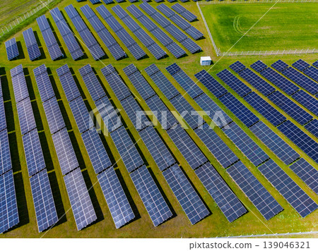 Large solar panel installation in a green field under bright sunlight with clear skies, showing rows of panels organized systematically for energy generation 139046321