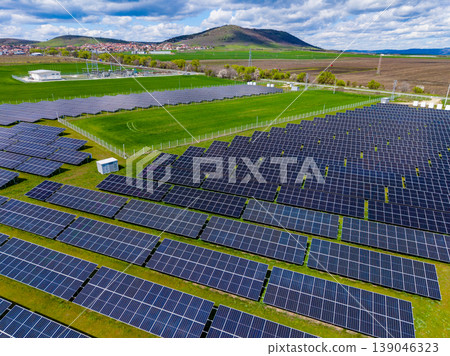 Solar panels cover land in a renewable energy farm located in a rural area with hills in the background during daytime under clouds Solar panels cover land in a renewable energy farm located in a rural area with hills in the background during daytime under clouds 139046323