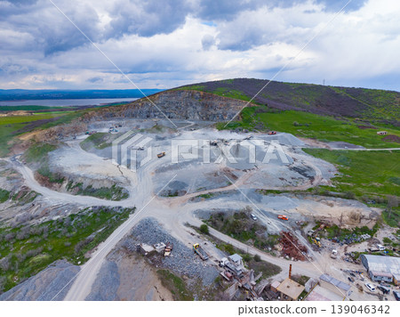 Granite quarry located in a rural area with heavy machinery and trucks engaged in stone extraction during cloudy weather Granite quarry located in a rural area with heavy machinery and trucks engaged in stone extraction during cloudy weather 139046342
