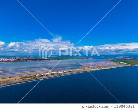 Bird's eye view of salt fields along a coastline near a city under a bright sky with clouds in the background during the day Bird's eye view of salt fields along a coastline near a city under a bright sky with clouds in the background during the day 139046351