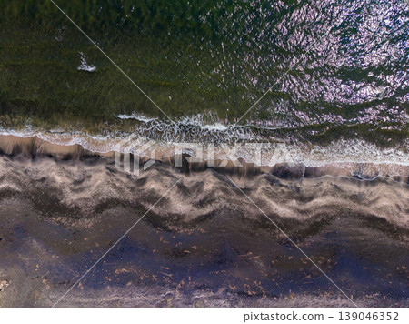 Waves meet the shore at a sandy beach in the afternoon sun with clear water and gentle ripples on the surface Waves meet the shore at a sandy beach in the afternoon sun with clear water and gentle ripples on the surface 139046352