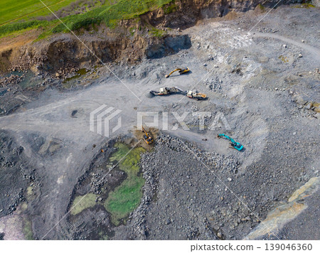 Granite quarry site showing heavy machinery working and extracting stone in a large open area during daylight Granite quarry site showing heavy machinery working and extracting stone in a large open area during daylight 139046360