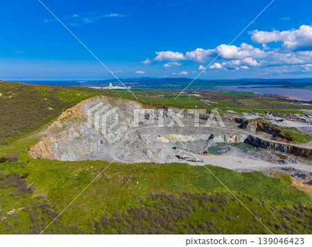 Granite quarry site showing large excavation area and machines working on the rock in the background near the hills and sky Granite quarry site showing large excavation area and machines working on the rock in the background near the hills and sky 139046423