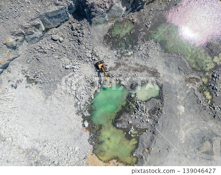 Granite quarry shows heavy machinery and water pools under clear sky during quarrying activity Granite quarry shows heavy machinery and water pools under clear sky during quarrying activity 139046427