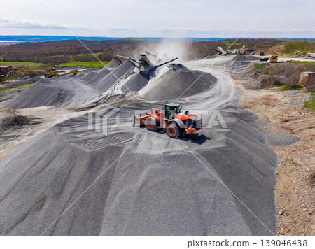 Workers operate heavy machinery at a granite quarry in a rural area during daylight hours while moving piles of crushed stone Workers operate heavy machinery at a granite quarry in a rural area during daylight hours while moving piles of crushed stone 139046438