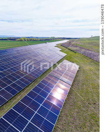 Solar panels cover a large area in a green field under bright skies during daytime near a rural location in an open landscape Solar panels cover a large area in a green field under bright skies during daytime near a rural location in an open landscape 139046478