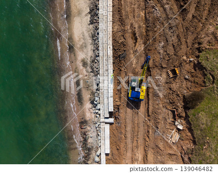 Construction of concrete structures along a beach at low tide with construction equipment and materials present on the ground Construction of concrete structures along a beach at low tide with construction equipment and materials present on the ground 139046482