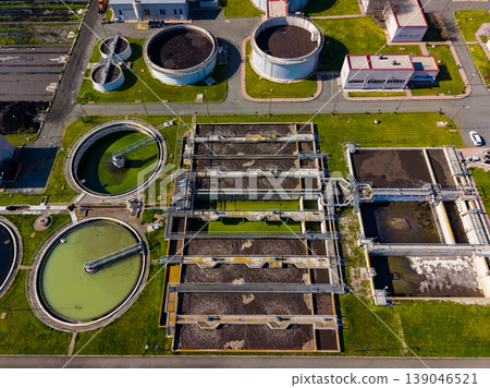 Water treatment facility processes wastewater on a sunny day with clear blue skies above and green grass surrounding the structures Water treatment facility processes wastewater on a sunny day with clear blue skies above and green grass surrounding the structures 139046521