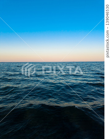 Sunset over the ocean with blue sky and calm water at the horizon viewed from the shore during the evening 139046530