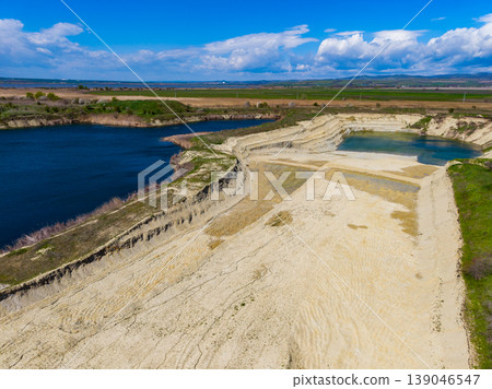 View of a sandy shore and blue waters located by a landscape with green hills and fields under a cloudy sky View of a sandy shore and blue waters located by a landscape with green hills and fields under a cloudy sky 139046547